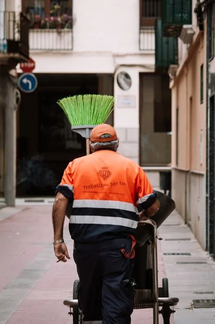 A man cleaning a glass barrier outdoors with a squeegee, surrounded by greenery.